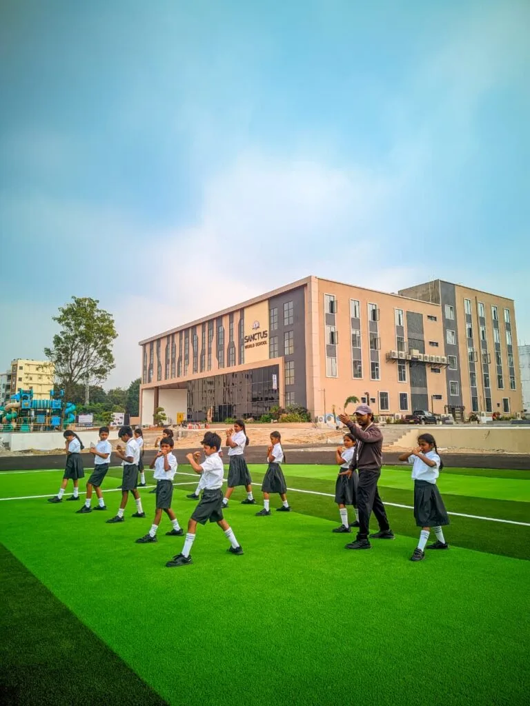 Large green outdoor sports area on the Sanctus World School campus in Shamshabad with students participating in physical education training